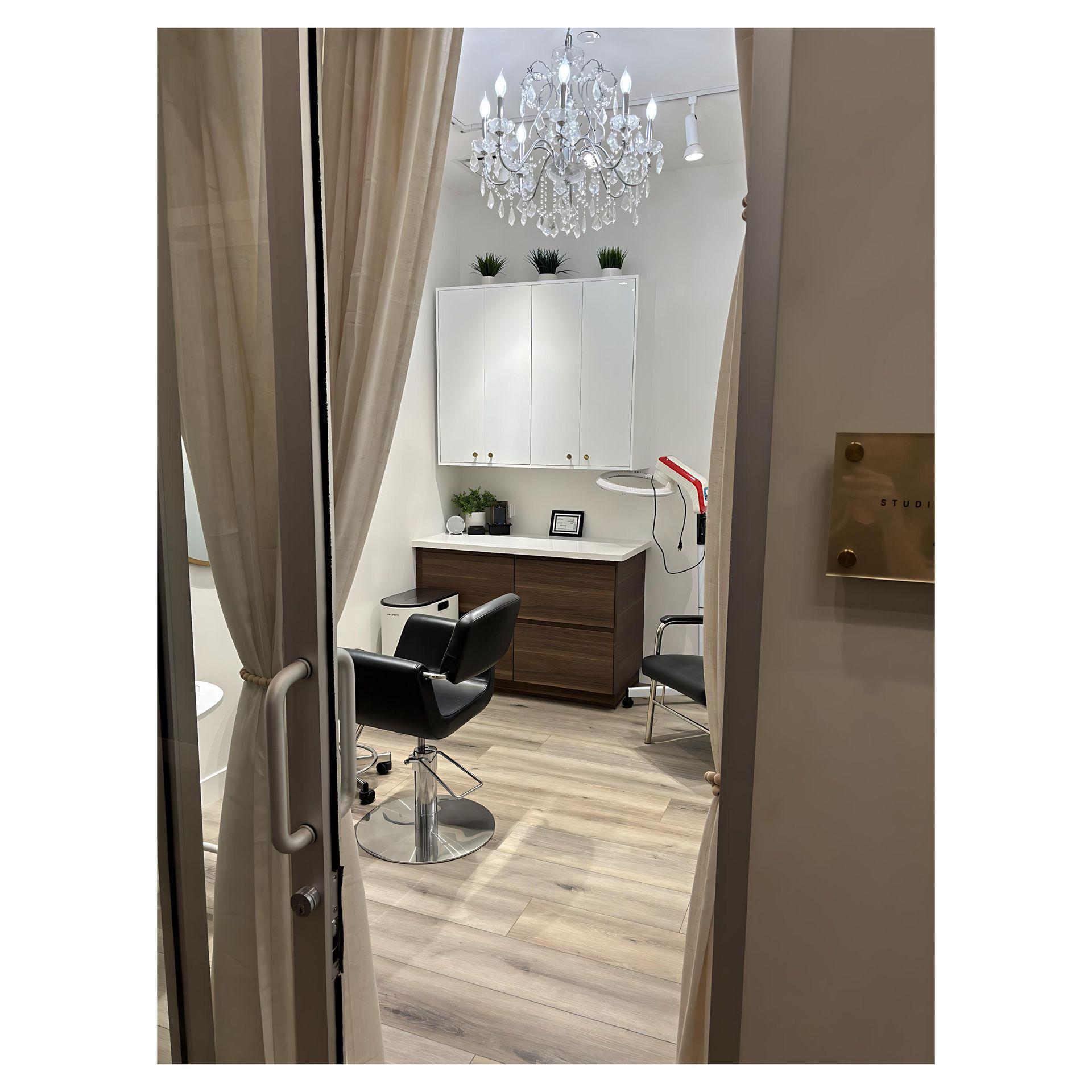 Modern salon interior with black chairs, chandelier, and wooden floor, viewed through open curtains.