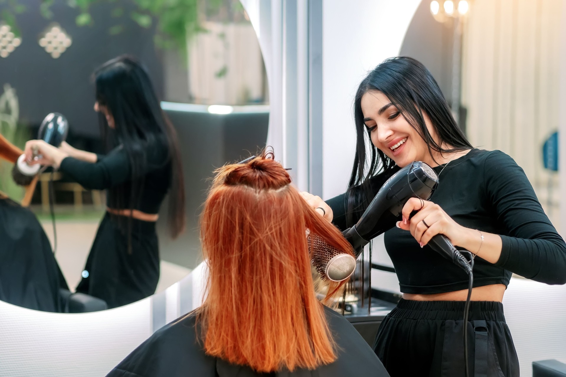 Hair styling in beauty salon. Woman does her hair in modern beauty salon. Woman stylist dries hair with hairdryer to salon client and smiles