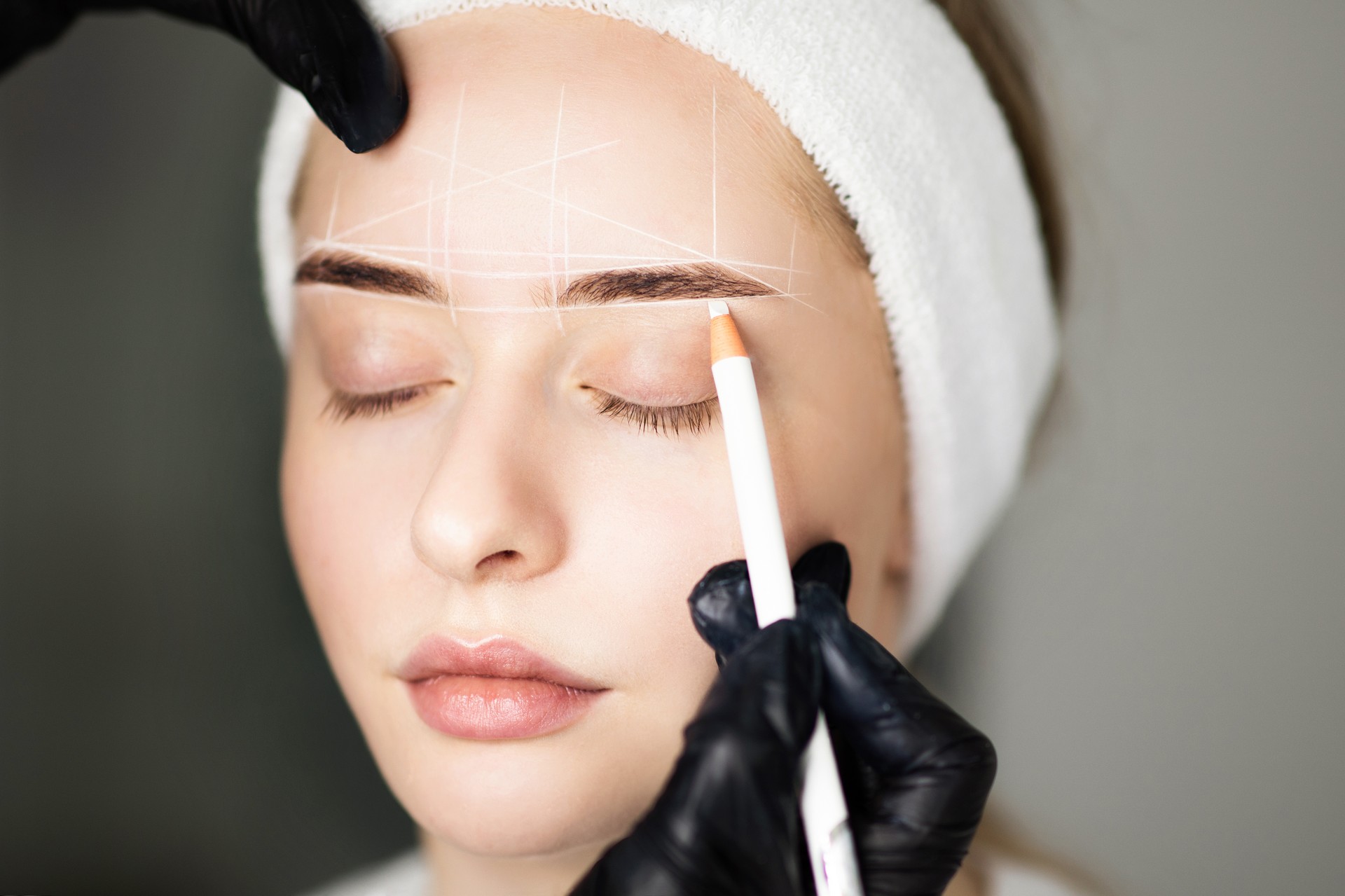 Cosmetologist Mapping Eyebrows Of Woman With White Pencil Before Permanent Makeup Treatment